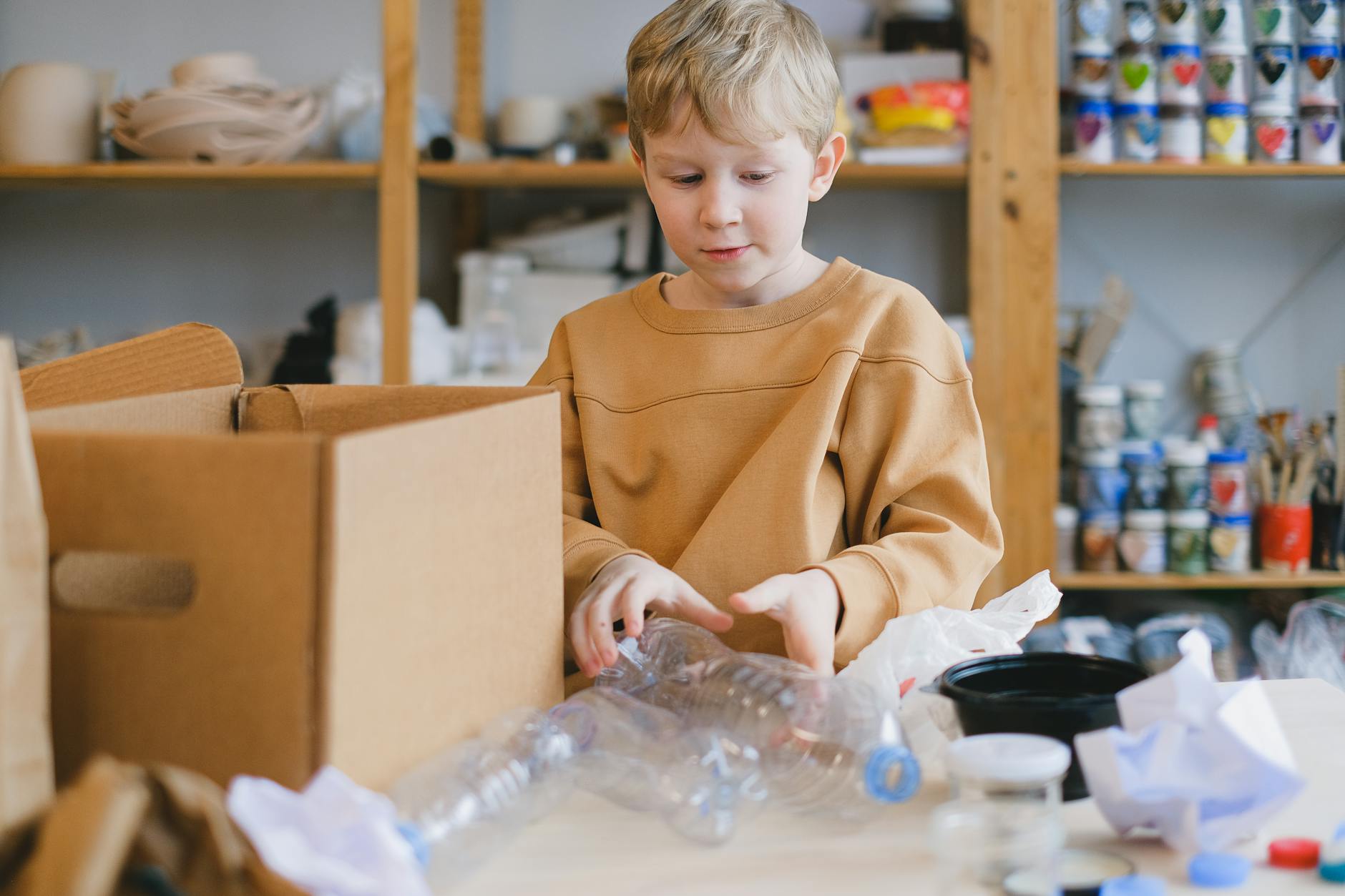 Chłopiec sortuje plastikowe butelki i kartony podczas nauki recyklingu