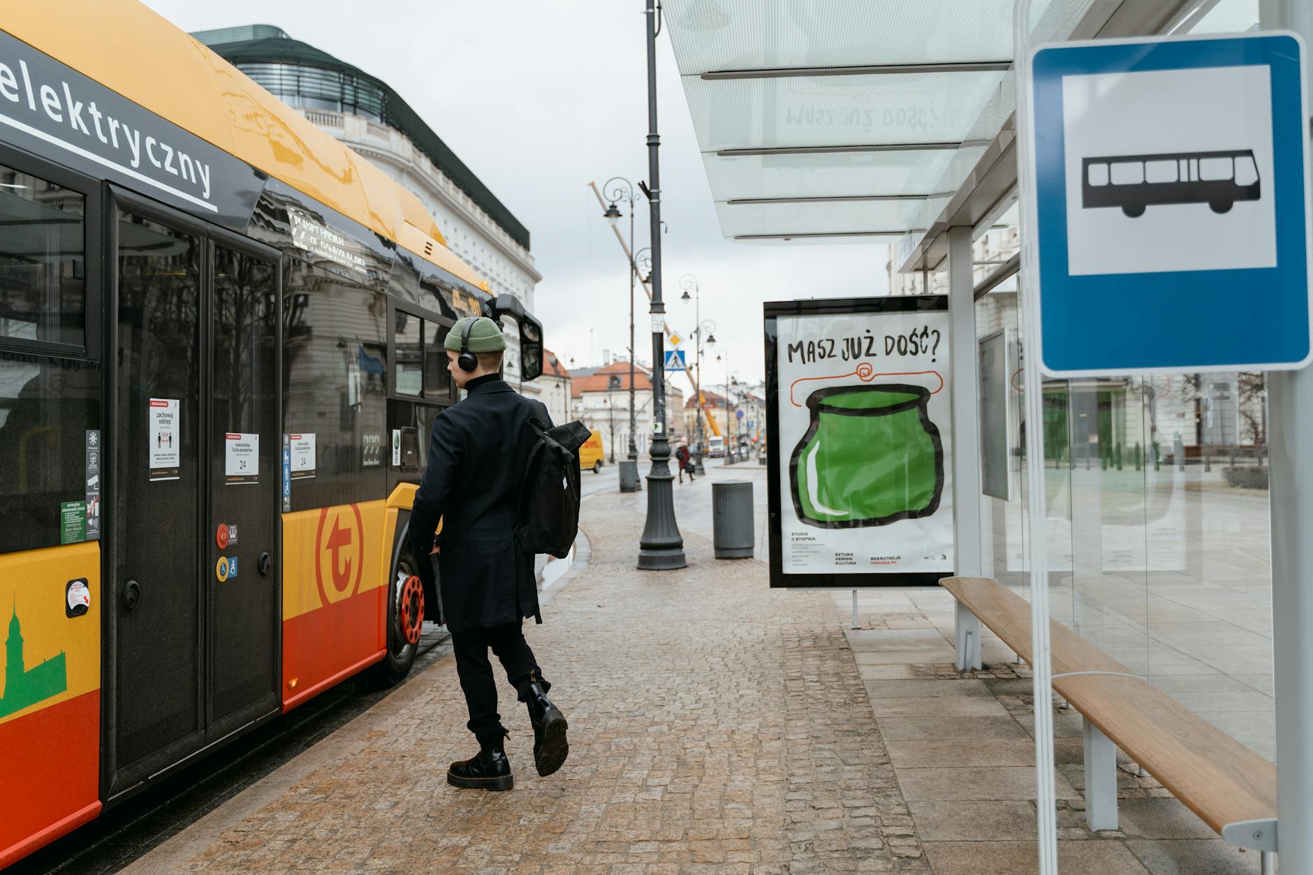 Ekokampania na przystanku: plakaty, hasła i zgody w przestrzeni publicznej Mężczyzna z plecakiem wsiada do elektrycznego autobusu na miejskim przystanku