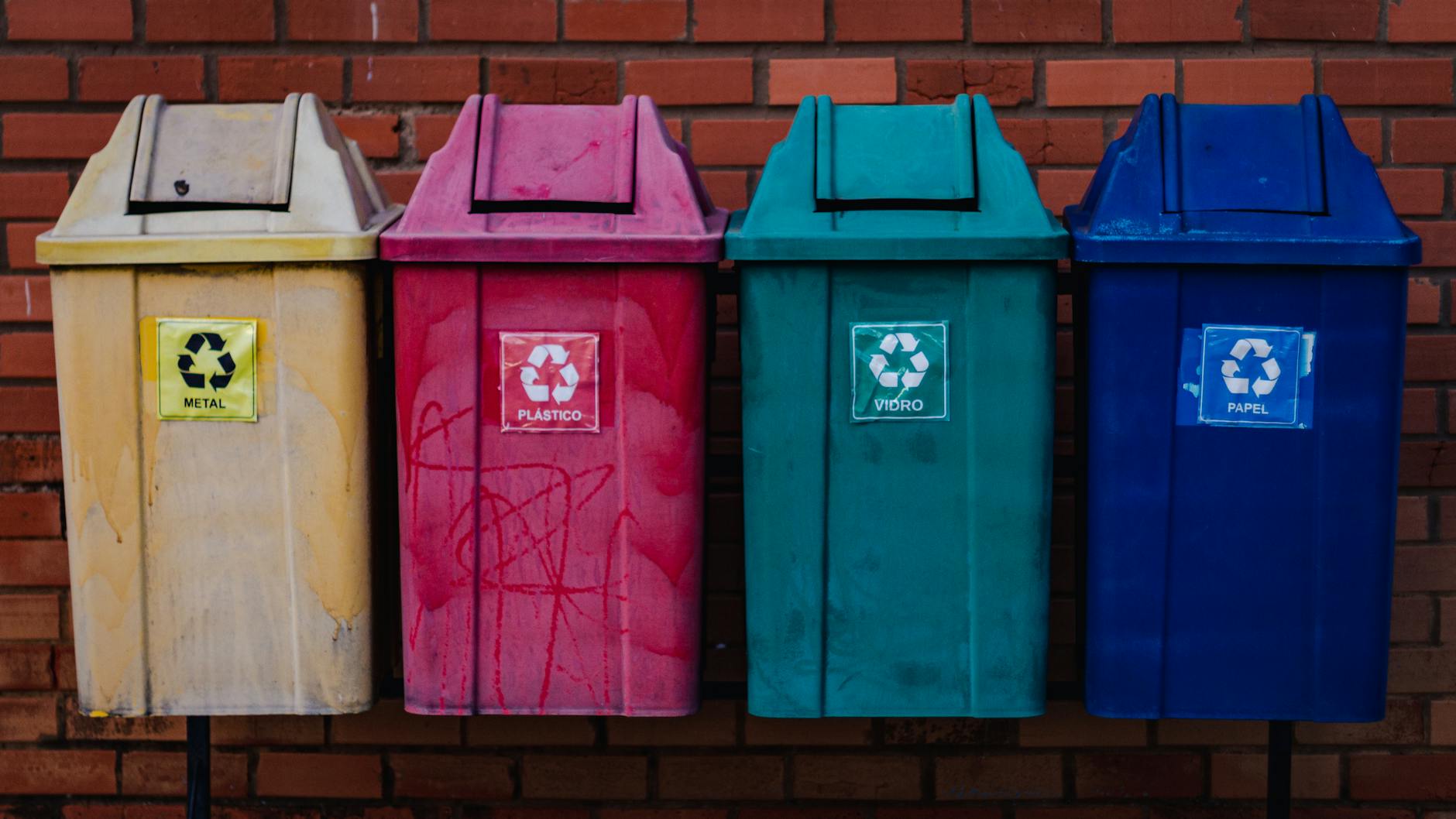 Cztery kolorowe pojemniki do recyklingu przy ceglanej ścianie szkoły