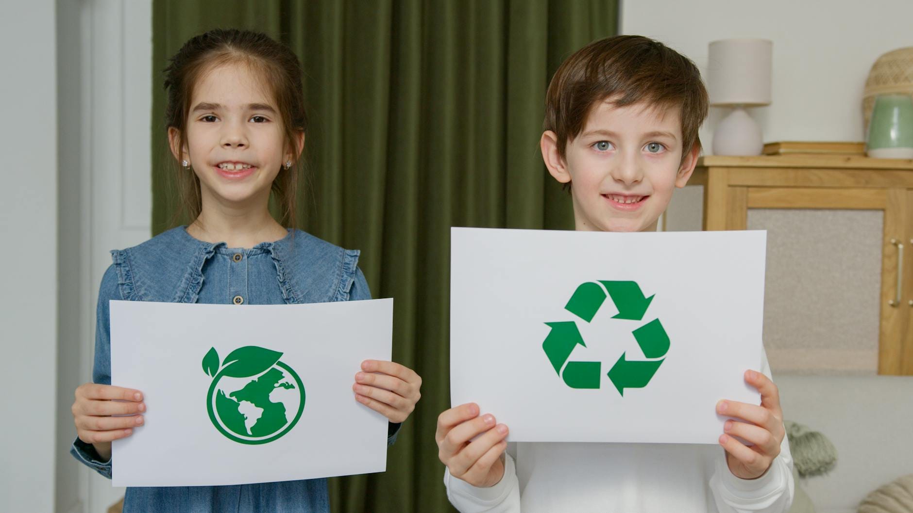 Dwoje dzieci w sali trzyma plakaty zachęcające do ekologii i recyklingu