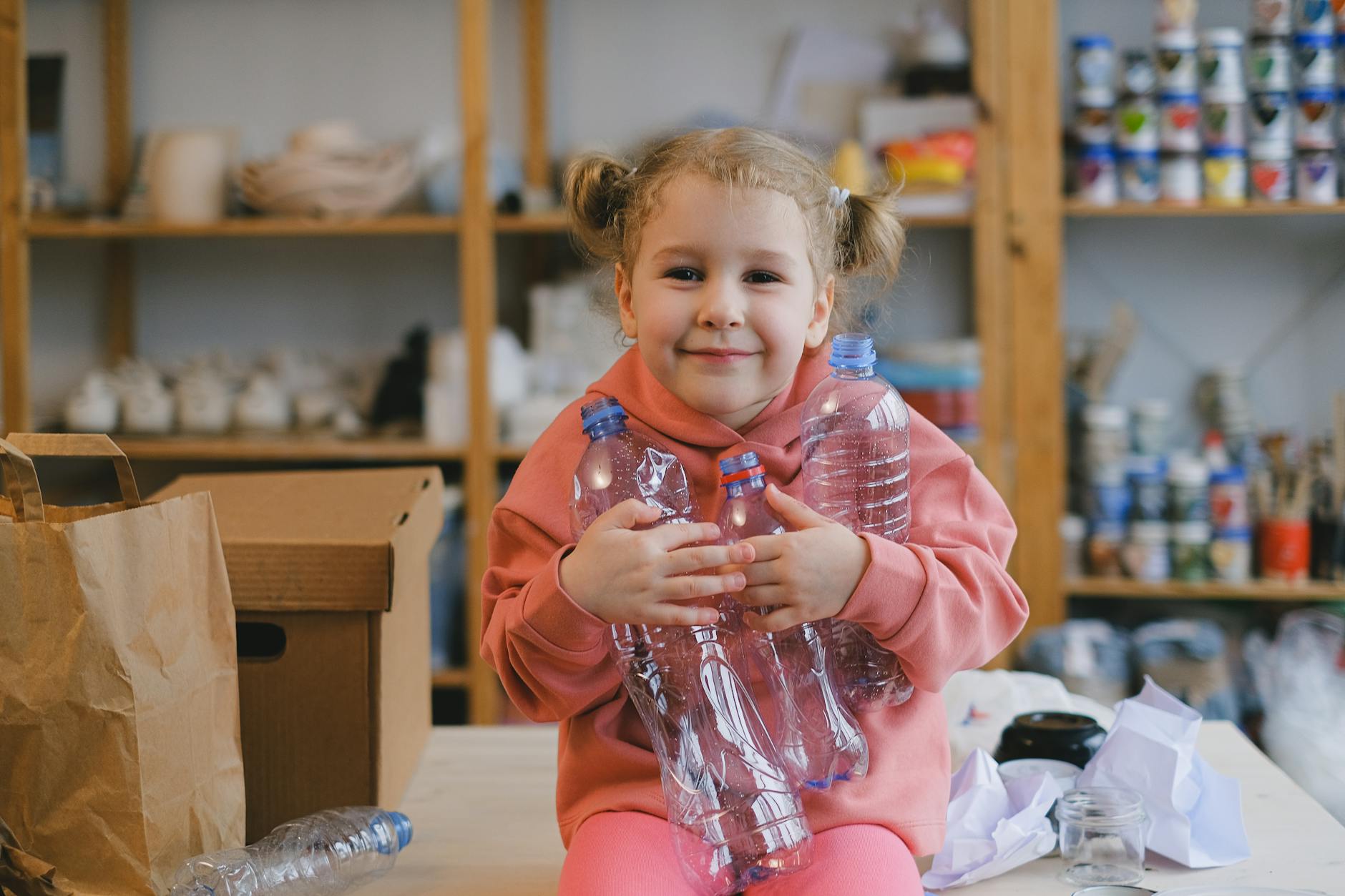 Dziewczynka w różowym swetrze trzyma plastikowe butelki do recyklingu