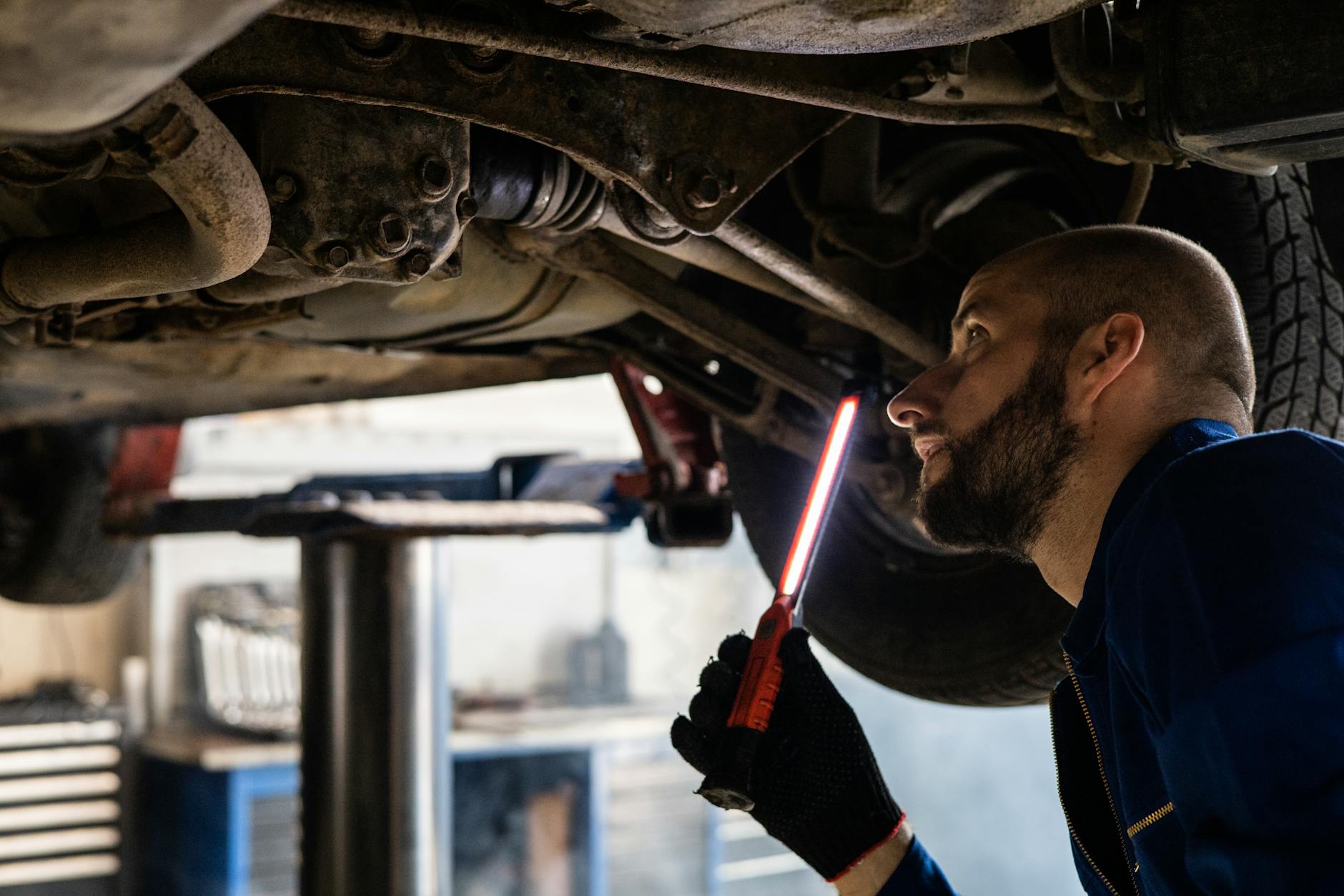 Mechanik z latarką sprawdzający podwozie auta w warsztacie