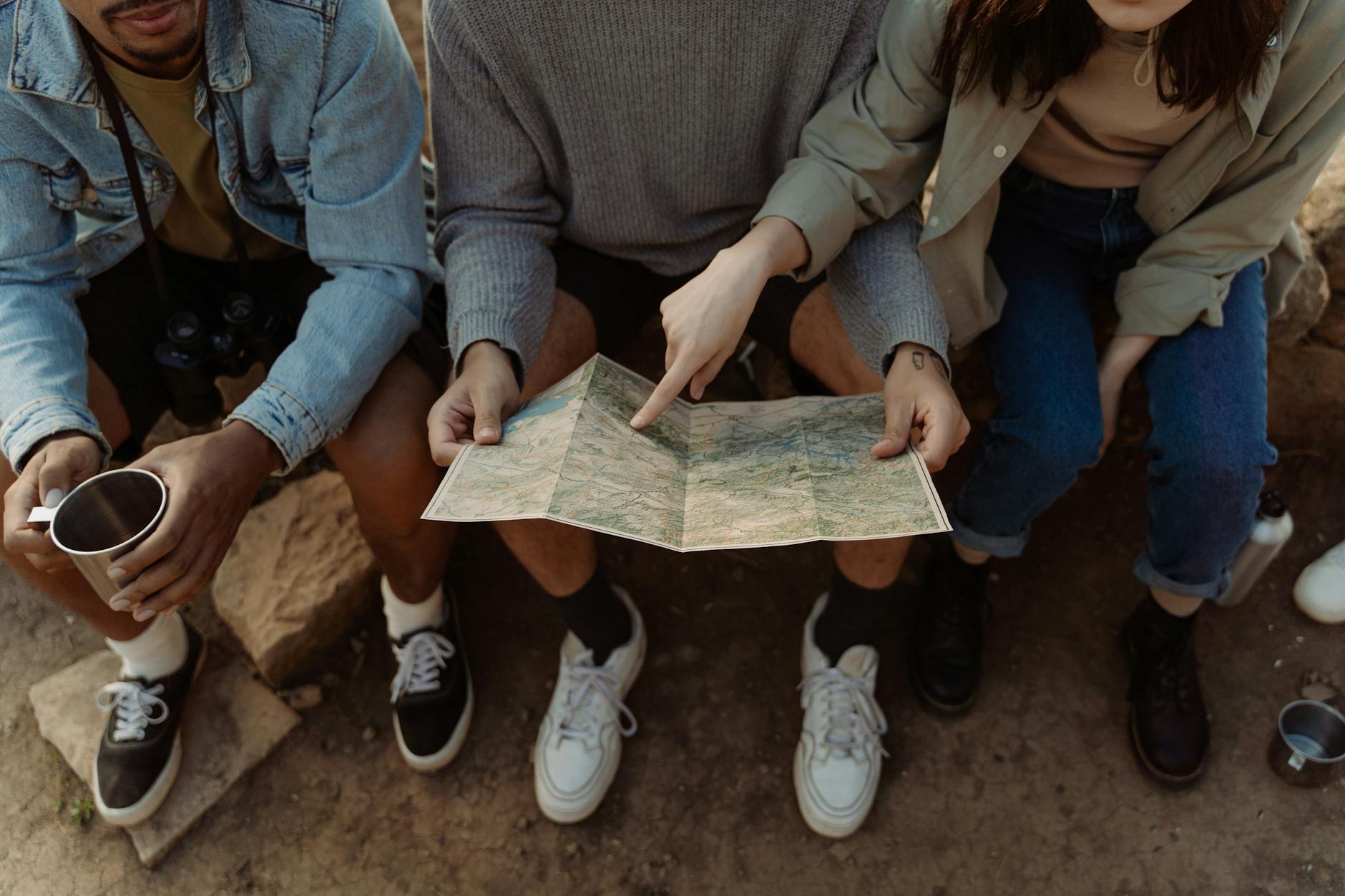 Uczniowie siedzący razem na trawie i wspólnie oglądający mapę Uczniowie siedzący razem na trawie i wspólnie oglądający mapę