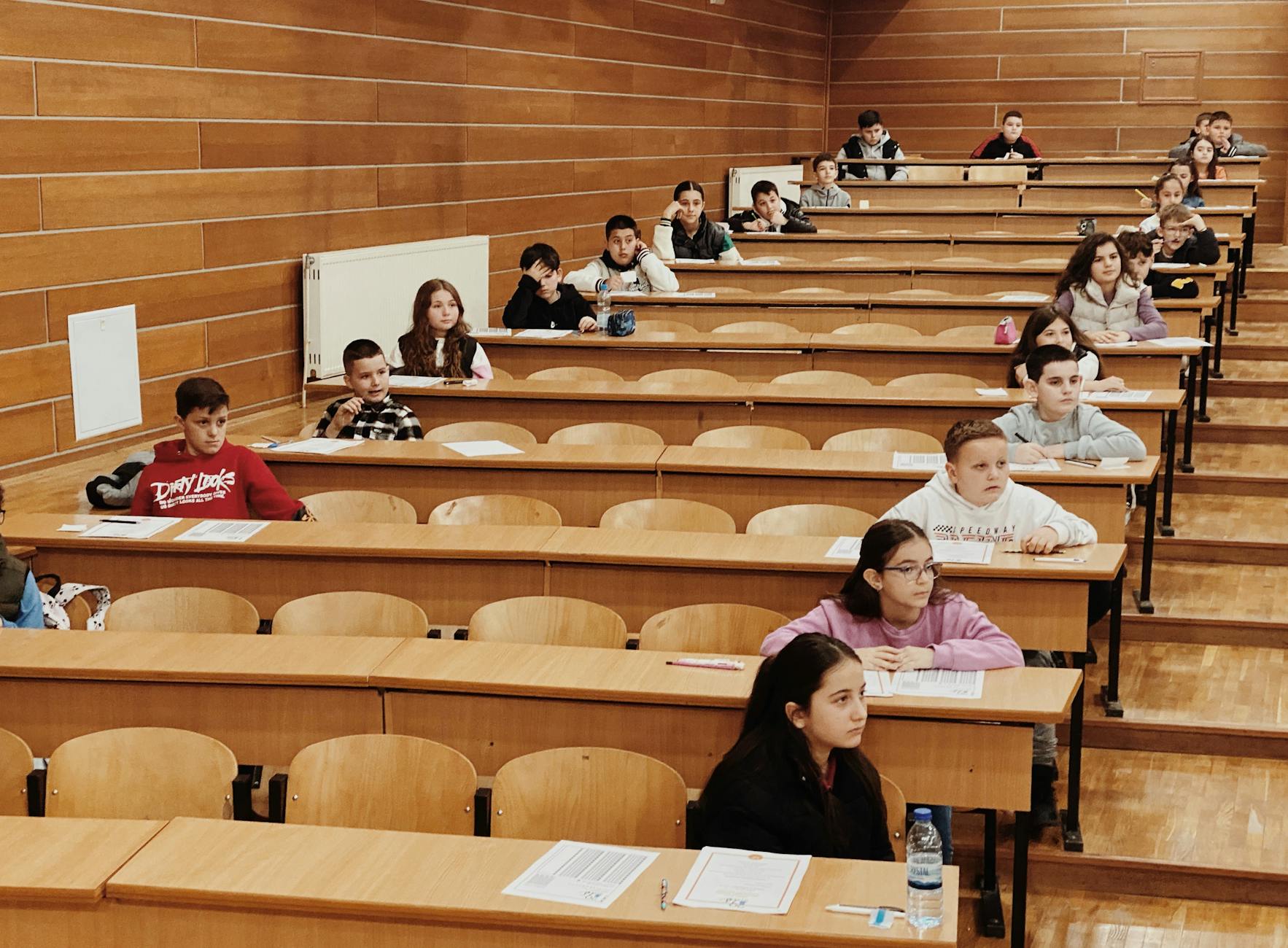 Uczniowie w ławkach piszą test w dużej sali wykładowej