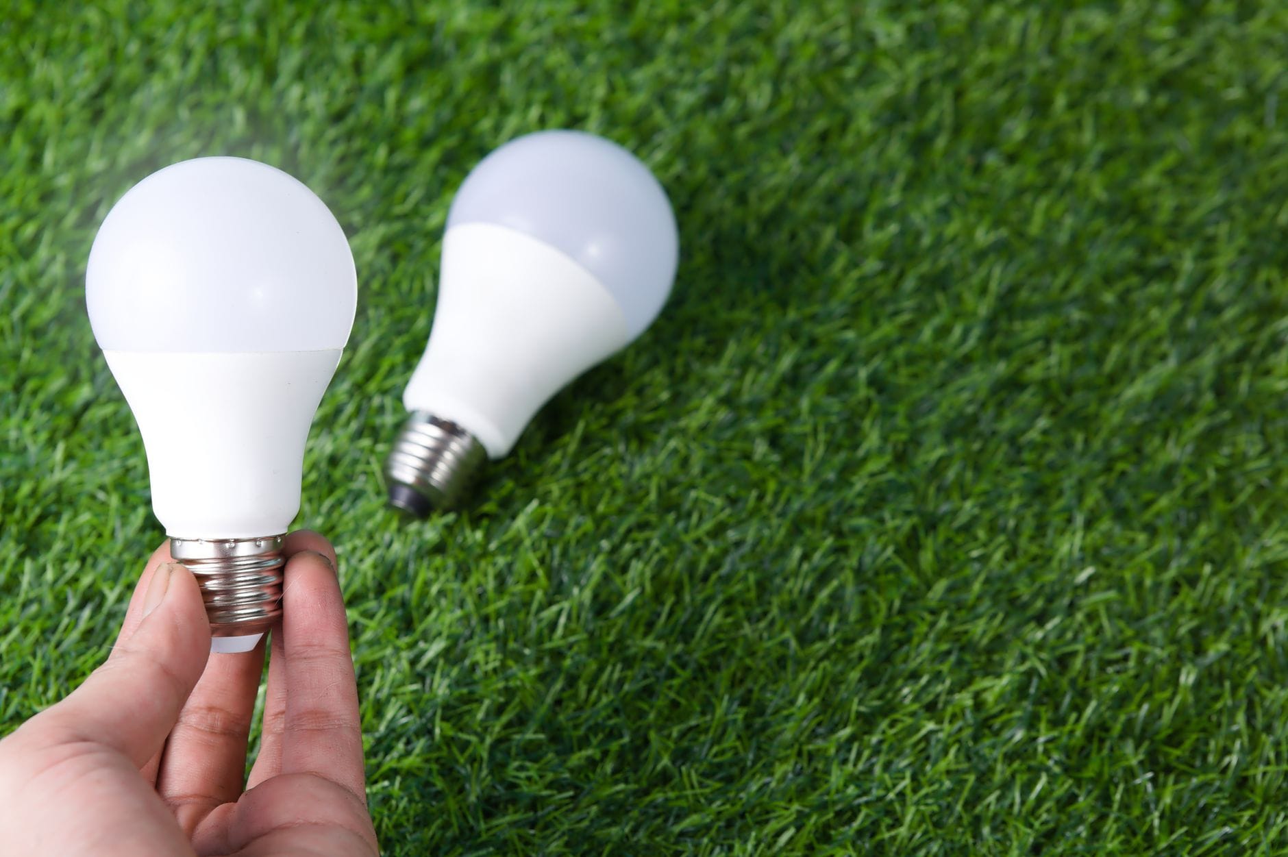 Dłoń trzyma żarówkę LED na trawie, symbol oszczędzania energii
